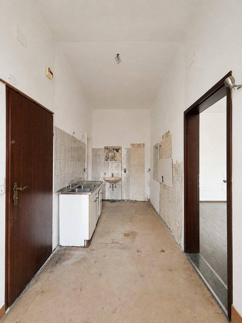 Renovierungsbedürftige Küche mit einfacher Spüle, kahlen Wänden und Betonboden.