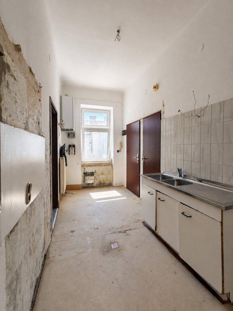 Sanierungsbedürftige Küche mit Fenster, Warmwasserbereiter und einfacher Spülenzeile.