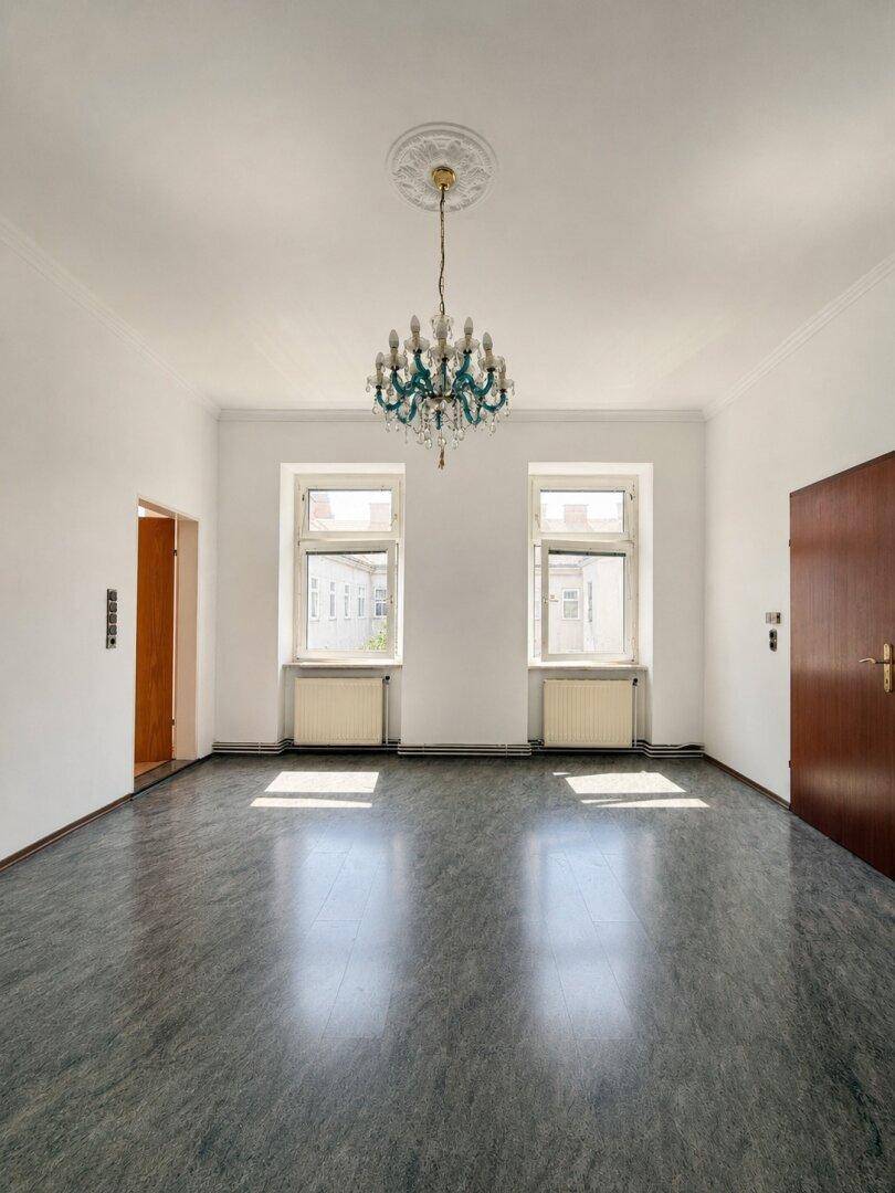Heller Wohnraum mit dunklem Linoleumboden, hohen Decken und einem dekorativen Kronleuchter.