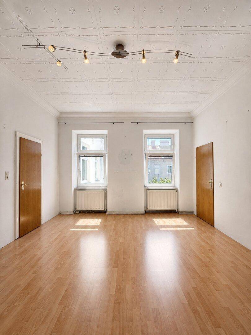 Geräumiger Raum mit hellem Laminatboden, zwei Fenstern und einer strukturierten Decke.