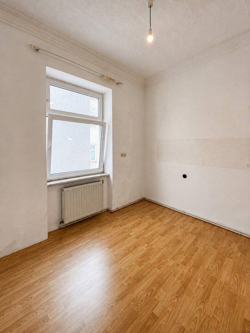 Helles Schlafzimmer mit Laminatboden, einem Fenster und Heizkörper, bereit zur Gestaltung.
