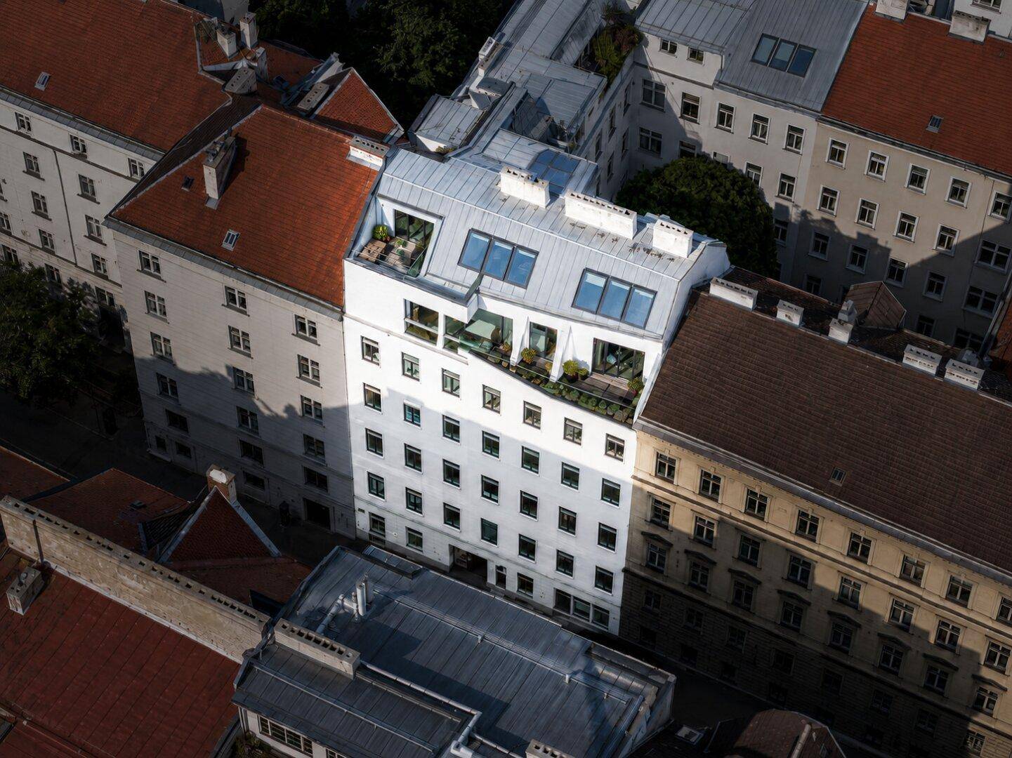 Luftaufnahme eines Stadtblocks mit verschiedenen Gebäuden, darunter ein modernes mit Dachterrassen.