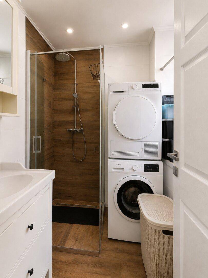 Funktionales Badezimmer mit Duschbereich, Waschbecken und praktischer Wasch-Trocken-Säule.