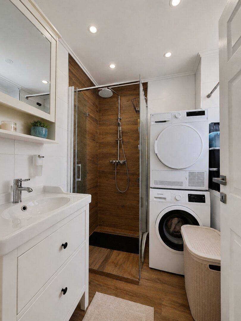 Modernes Badezimmer mit Duschkabine, Waschbecken und integrierter Waschmaschine und Trockner.