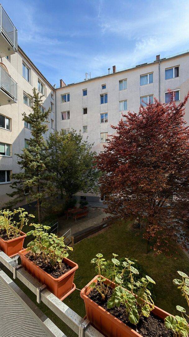 Blick vom Balkon mit Blumenkästen auf den grünen Innenhof und die umliegenden Wohngebäude.