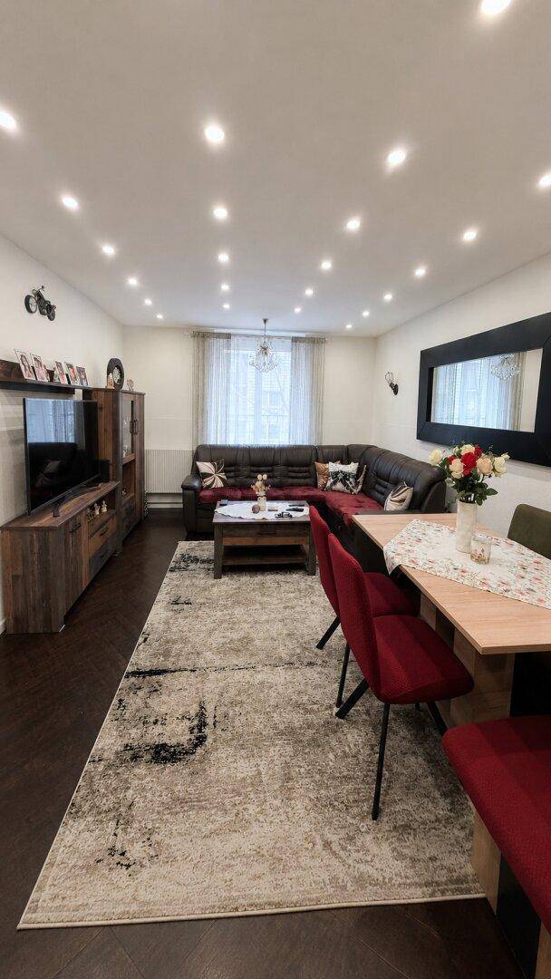 Gemütlicher Wohn-Essbereich mit dunklem Sofa, Esstisch und einem großen Teppich.