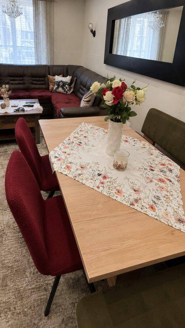 Essbereich mit Holztisch und roten Stühlen, dekoriert mit frischen Blumen.