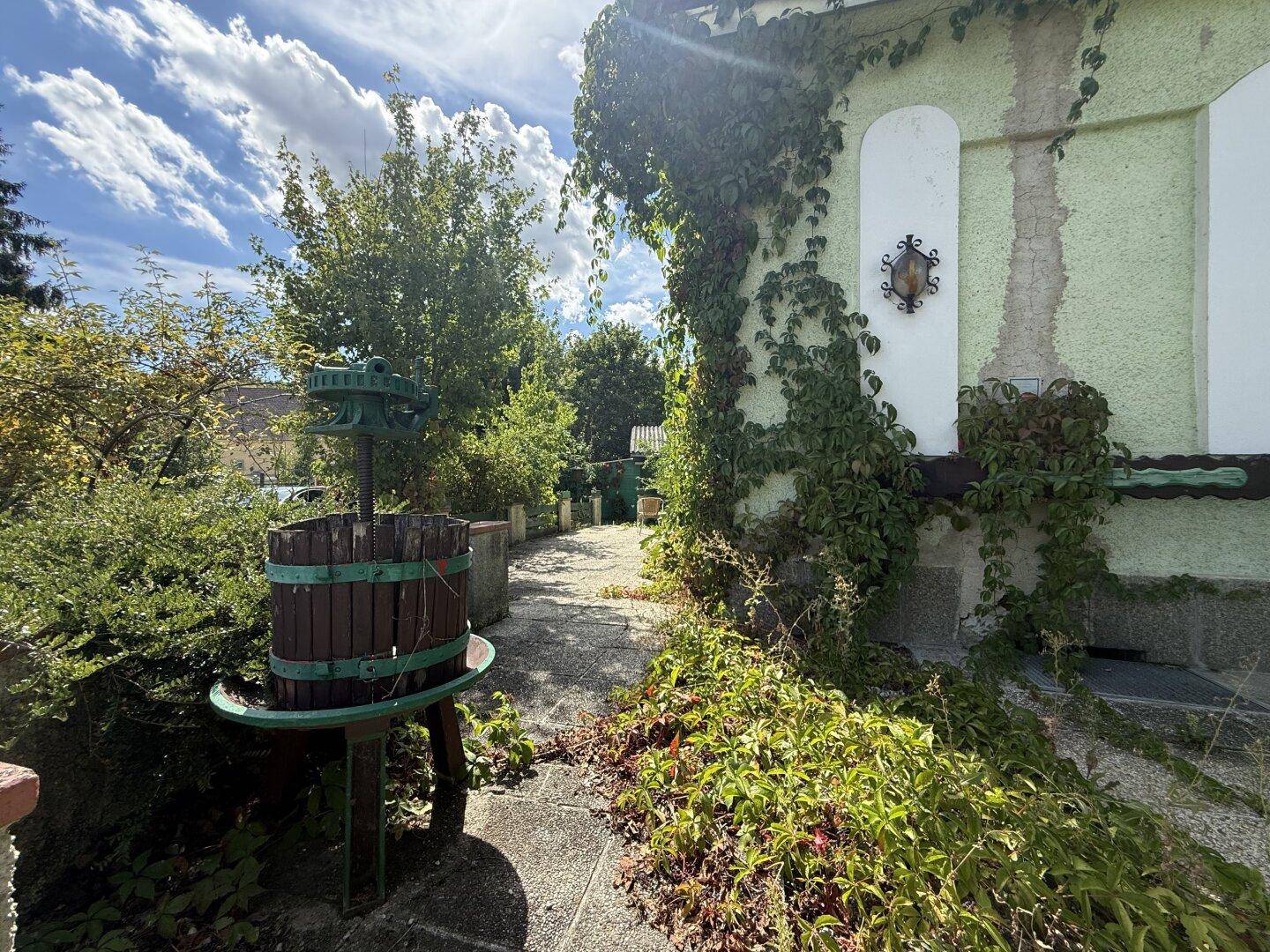 Gartenweg zum Haus mit einem dekorativen Holzfass und üppiger Vegetation.