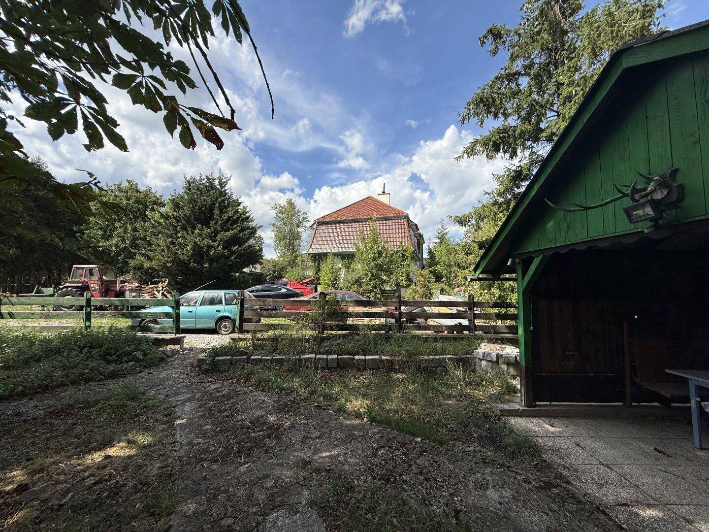 Weitläufiges Grundstück mit einem grünen Schuppen, geparkten Autos und dem Haupthaus im Hintergrund.
