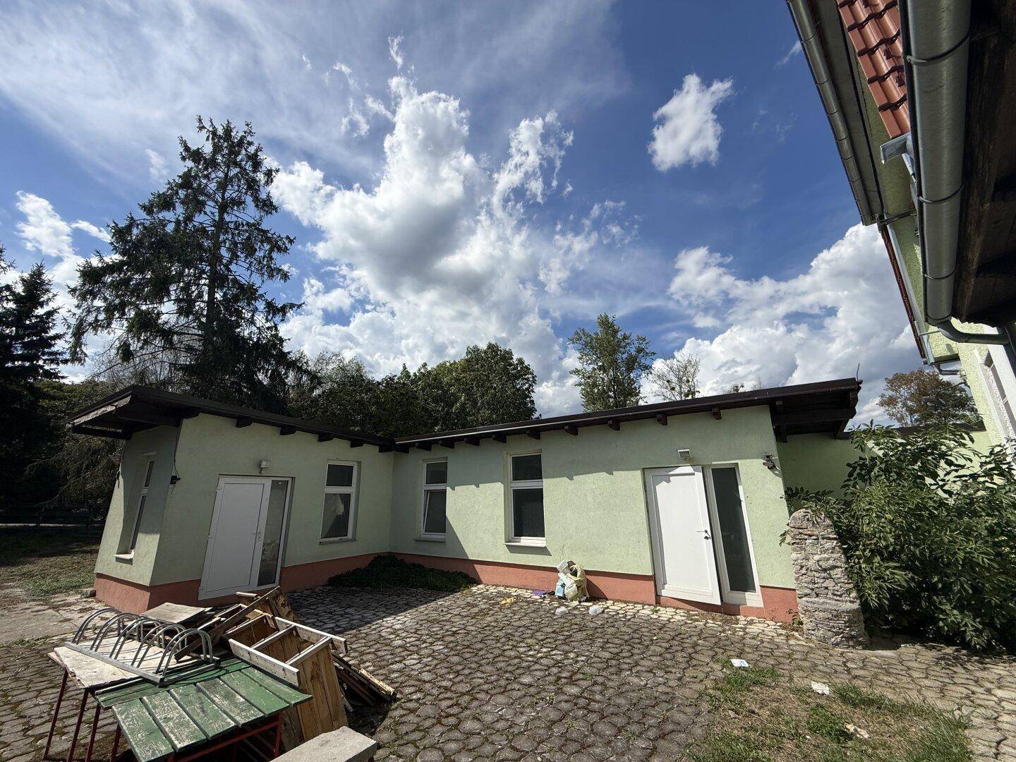 Anbau des Hauses mit mehreren Türen und Fenstern, umgeben von einem gepflasterten Bereich.