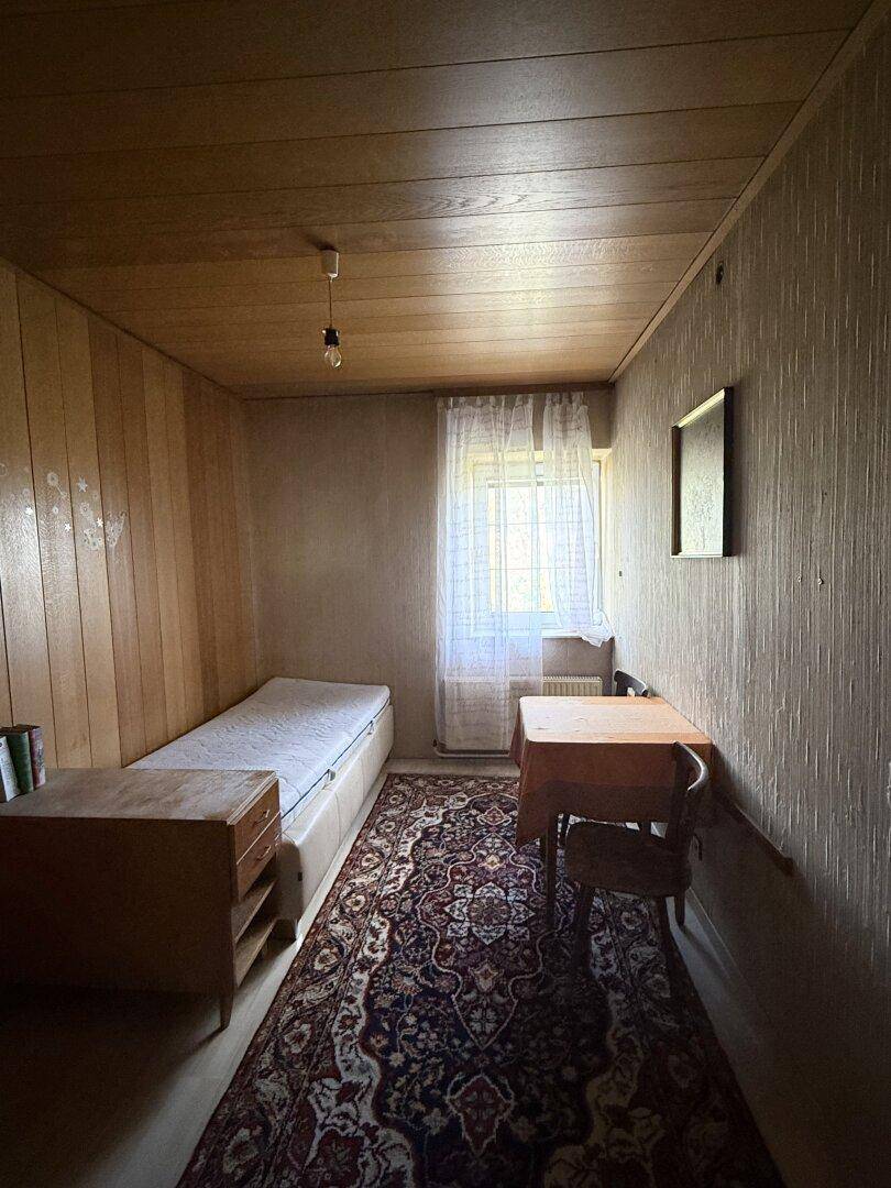 Einfaches Schlafzimmer mit Holzvertäfelung, Einzelbett und Teppichboden.