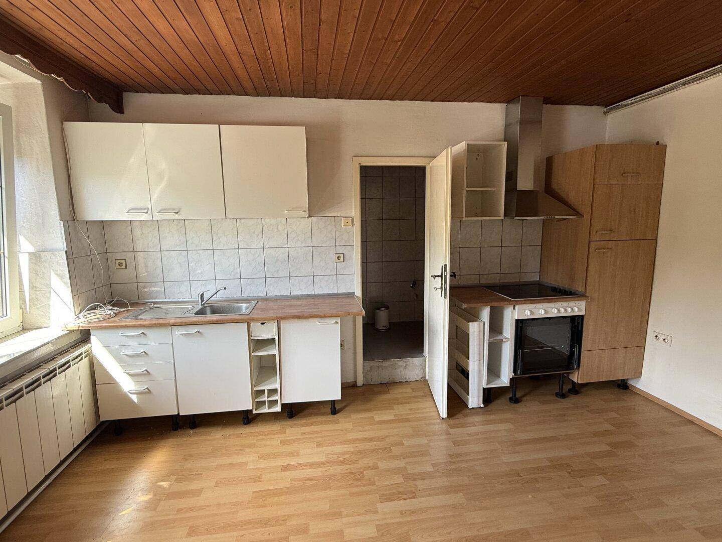 Einfache Küche mit weißen Schränken, Herd und Holzdecke, bereit zur Modernisierung.
