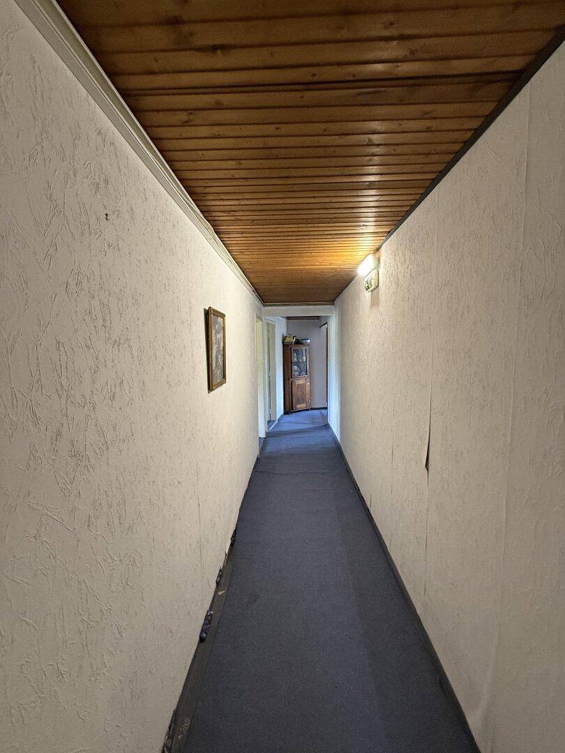 Schmaler Flur mit Teppichboden und Holzdecke, verbindet verschiedene Bereiche des Hauses.
