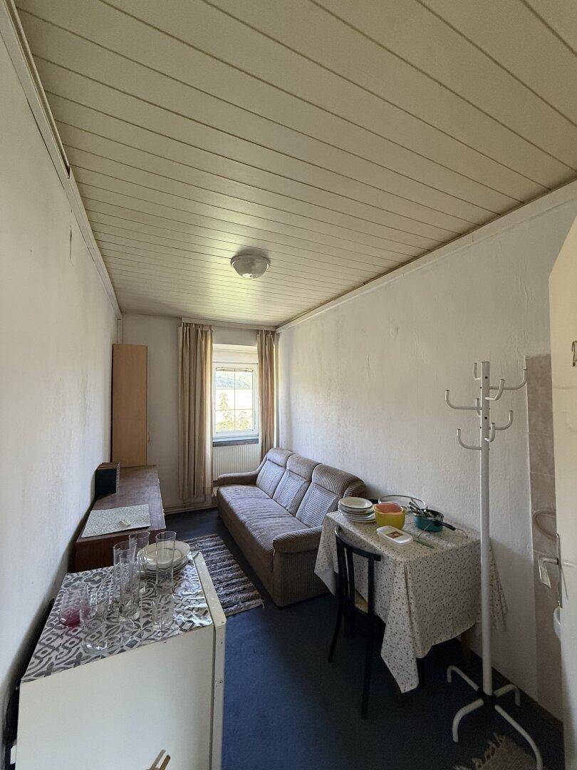 Kleiner Wohnbereich mit Sofa, Esstisch und weiß gestrichener Holzdecke, mit Fenster.
