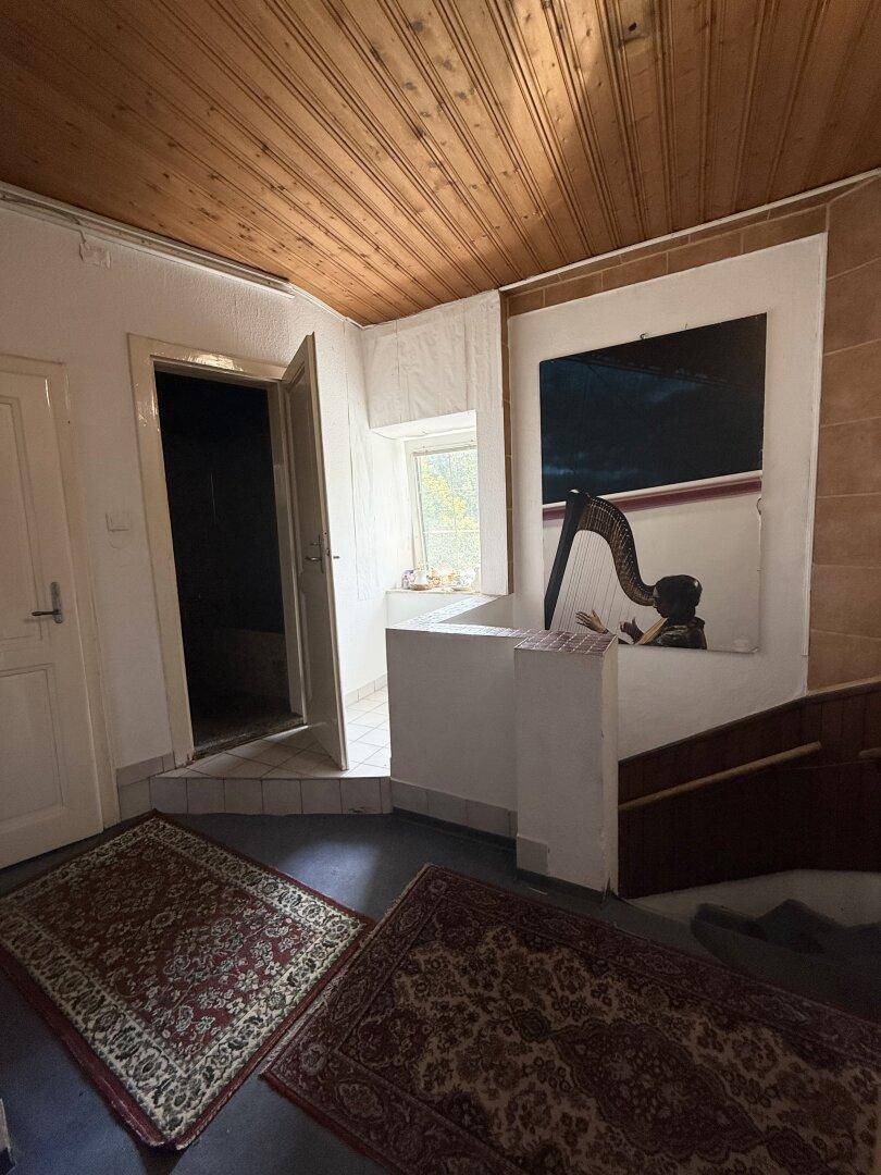Bereich mit Teppichen, kleinem Fenster und Tür zu einem Nebenraum, mit Holzdecke.