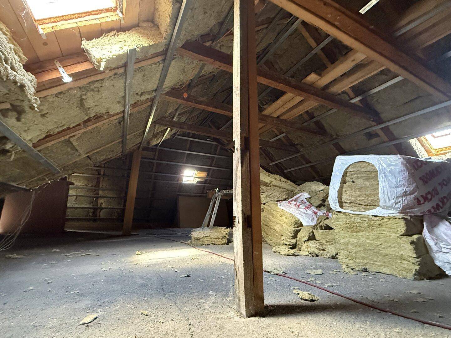 Geräumiger Dachboden mit Isolierung und Holzbalken, ideal für zukünftige Wohnraumerweiterung.