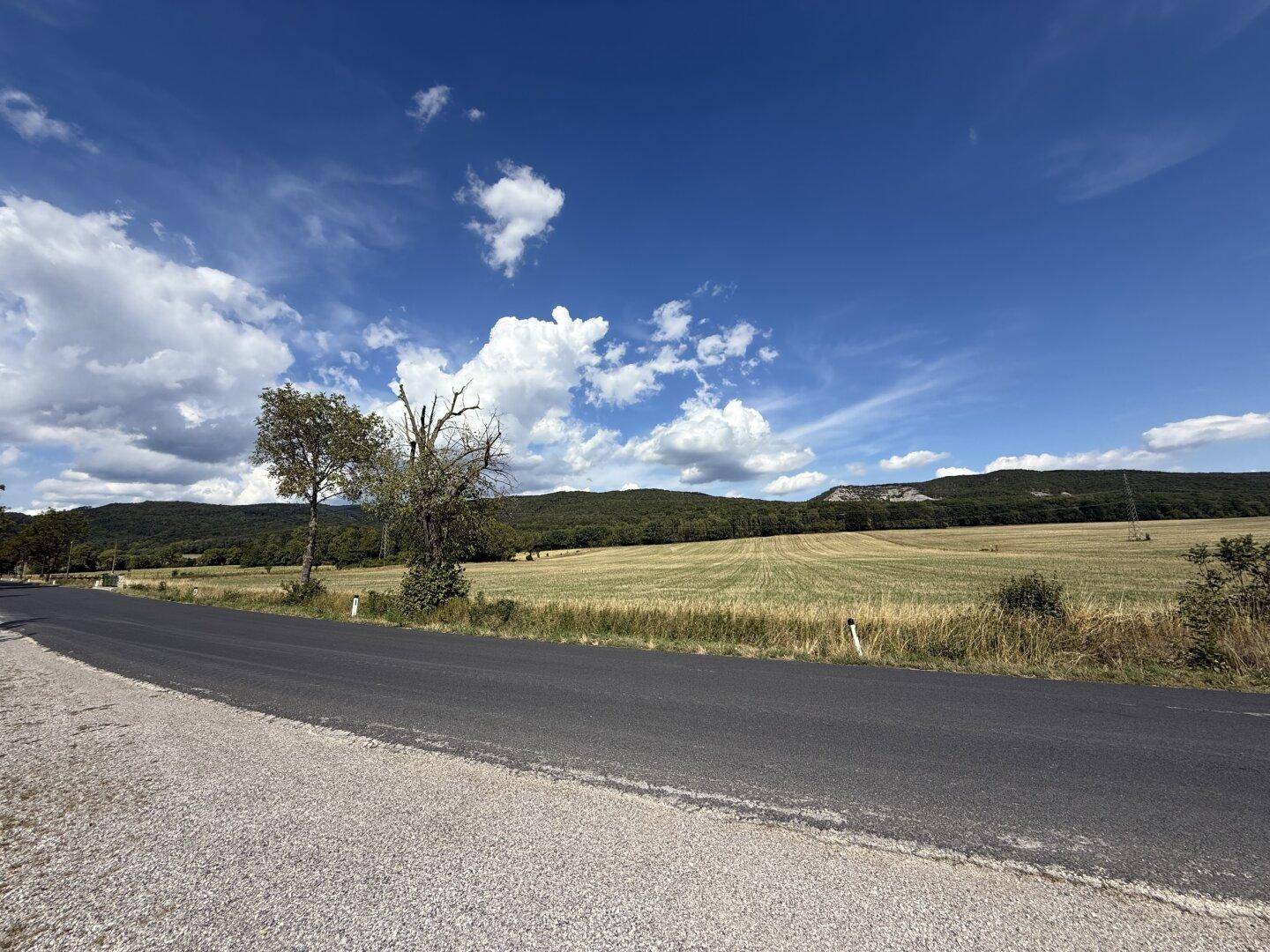 Malerische Landschaft mit Feldern, Hügeln und blauem Himmel, entlang einer Landstraße.
