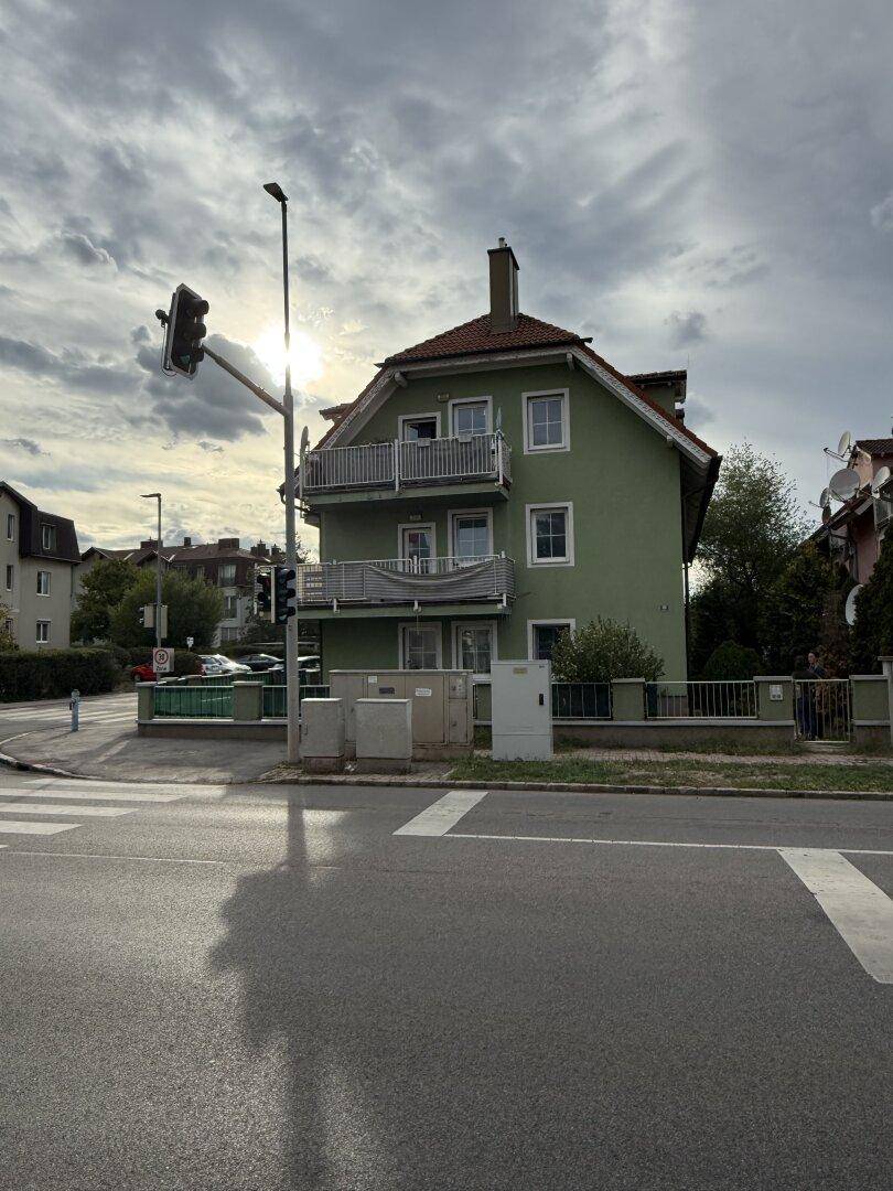 Grüne Hausfassade mit roten Ziegeldächern und Balkonen, aufgenommen bei bewölktem Himmel.