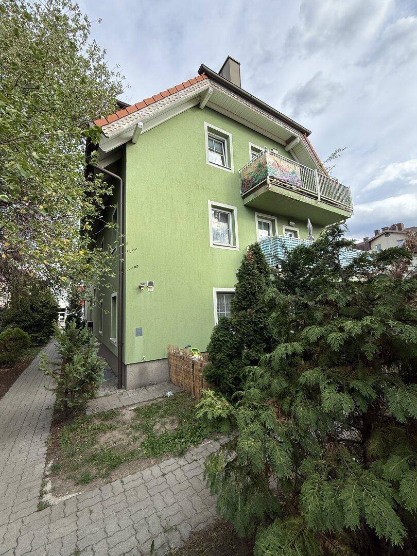 Seitenansicht des grünen Gebäudes mit einem Balkon und umgebender Vegetation.