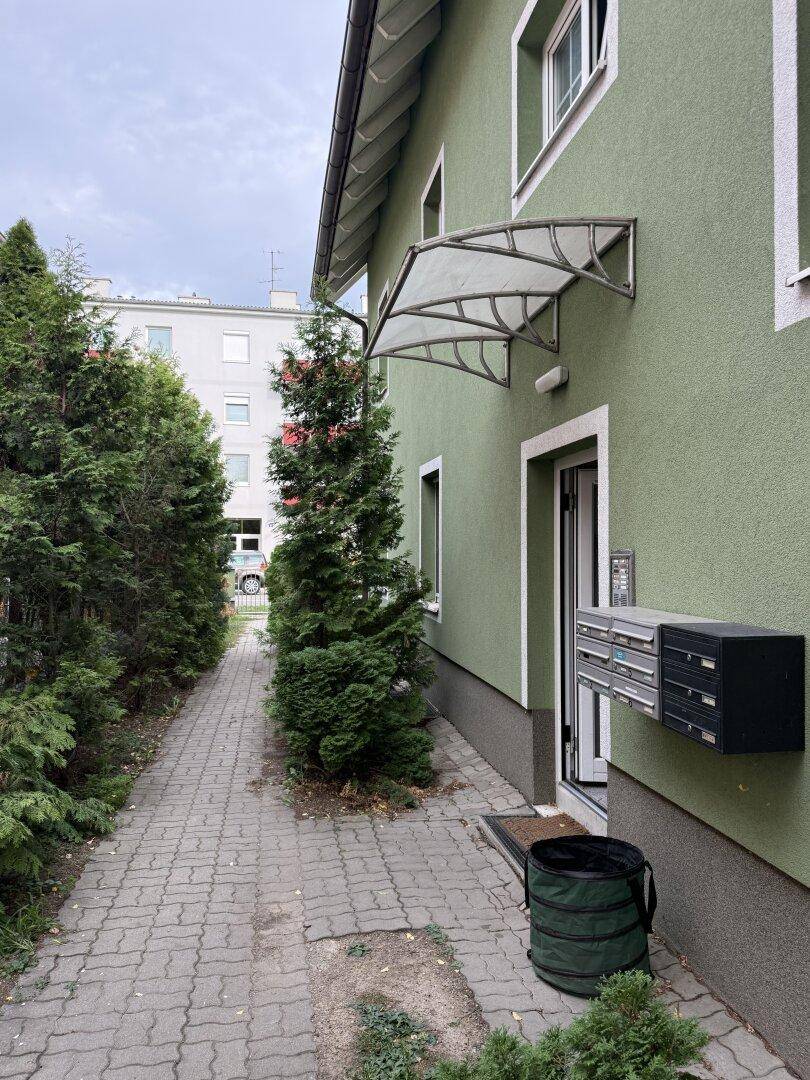 Eingangsbereich des Gebäudes mit Briefkästen, einer Überdachung und einem gepflasterten Weg.