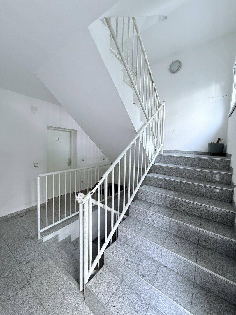 Helles Treppenhaus mit gefliesten Stufen und weißem Geländer in einem Mehrfamilienhaus.