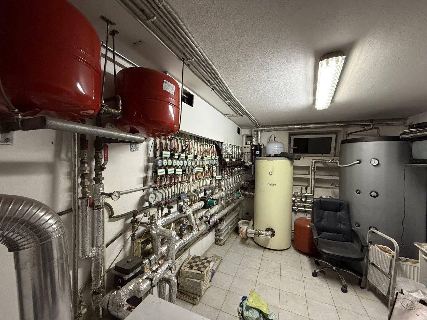 Heizungsraum mit mehreren Warmwasserspeichern, Rohren und technischen Installationen.