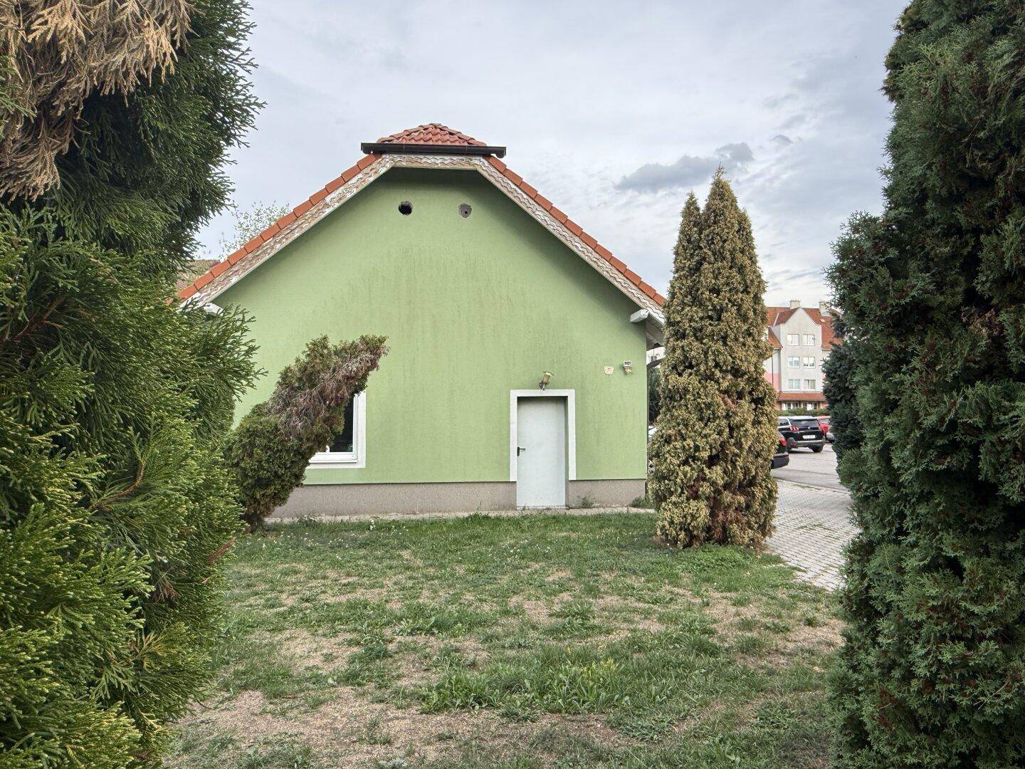 Rückseite des Nebengebäudes mit grüner Fassade, einer Tür und Rasenfläche.