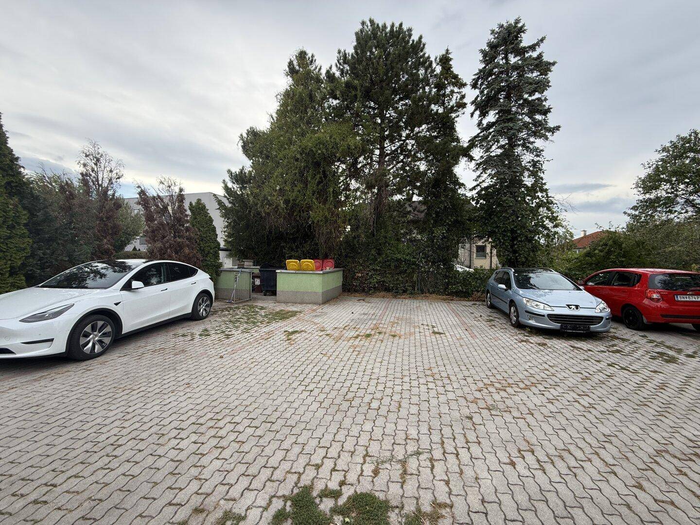 Großer Außenparkplatz mit mehreren geparkten Autos und umgebenden Bäumen.