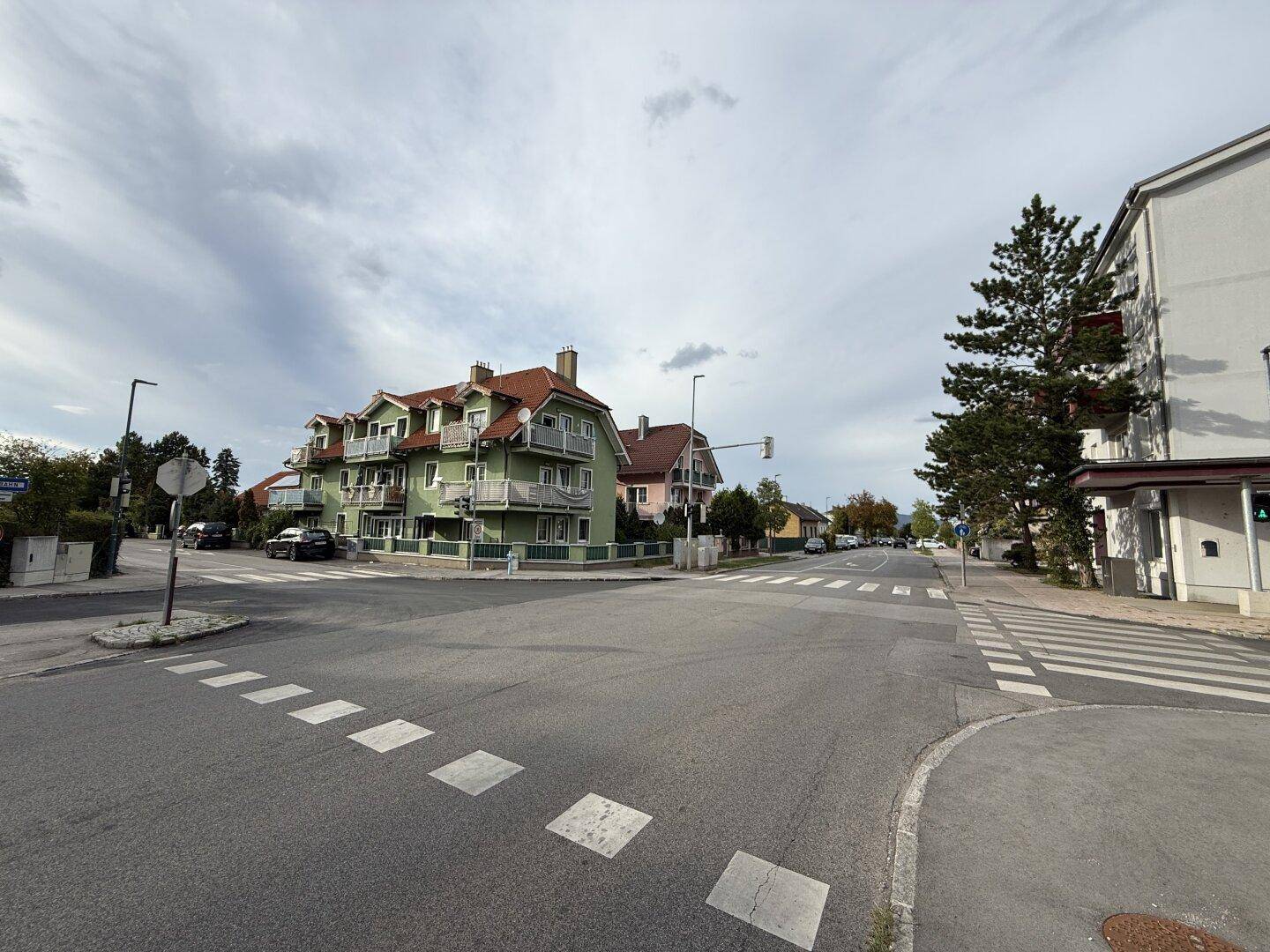 Weitläufige Straßenansicht mit dem grünen Mehrfamilienhaus an einer Kreuzung.