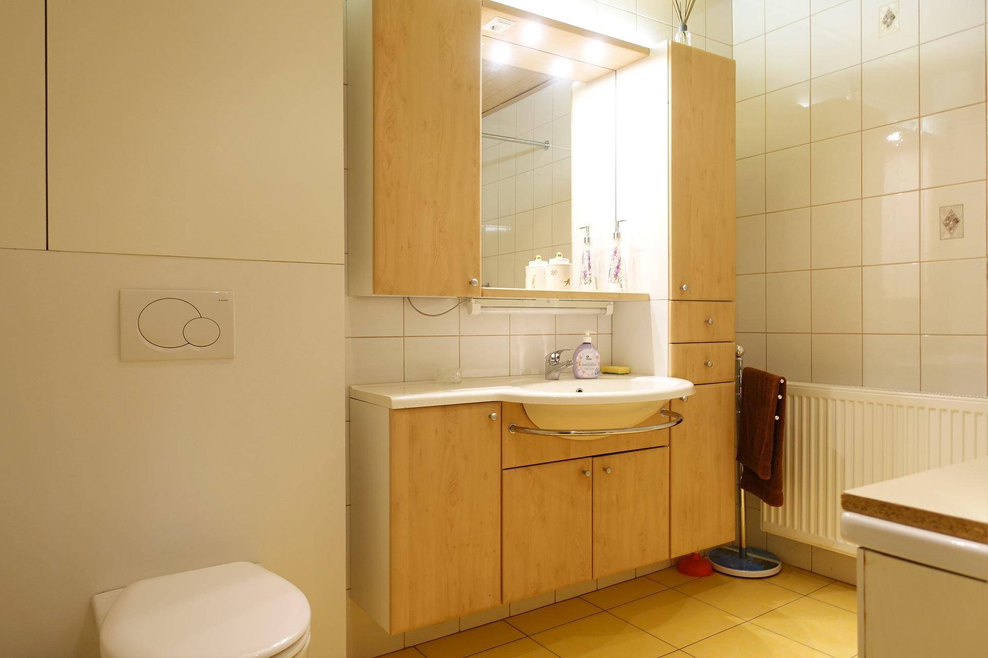 Badezimmer mit Waschbecken, Spiegelschrank und WC in hellen Fliesen.
