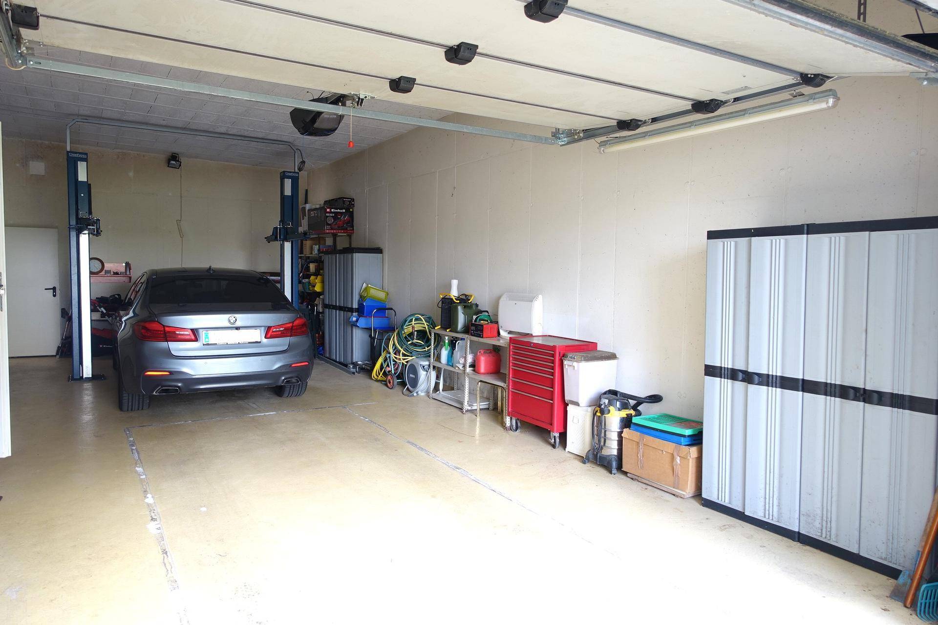 Geräumige Garage mit Hebebühne, einem Auto und viel Stauraum.