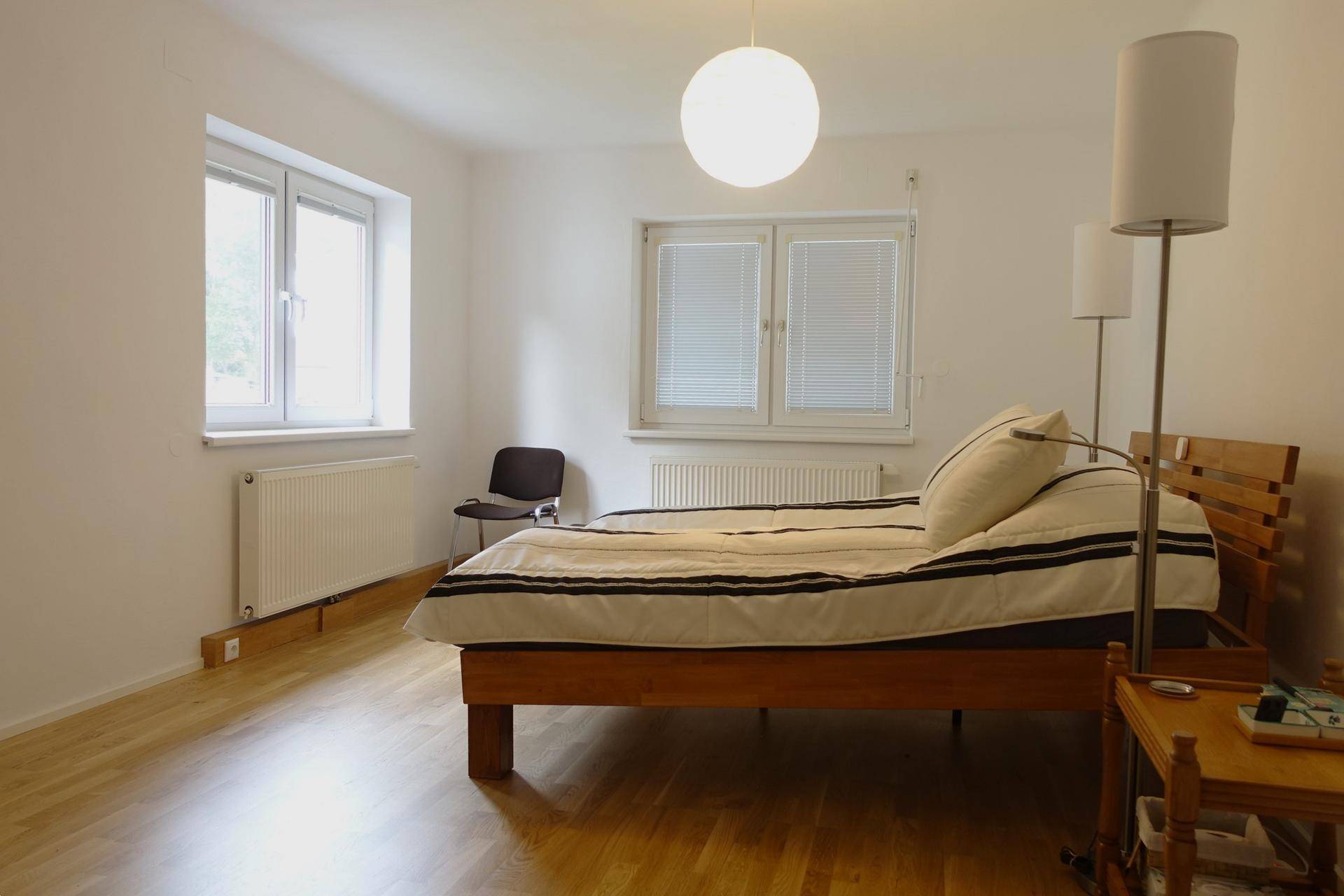 Schlafzimmer mit Doppelbett, zwei Fenstern und hellem Holzboden.