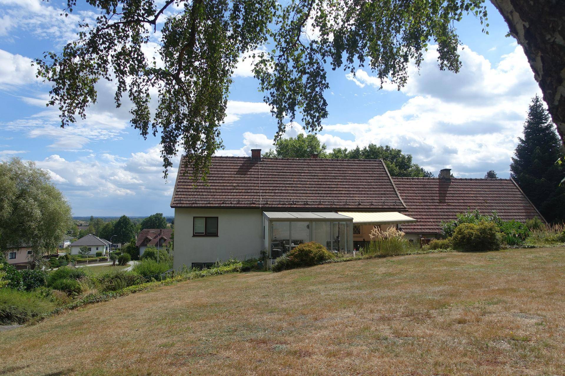 Rückseite des Hauses mit Wintergarten und weitläufiger Rasenfläche, Fernblick.
