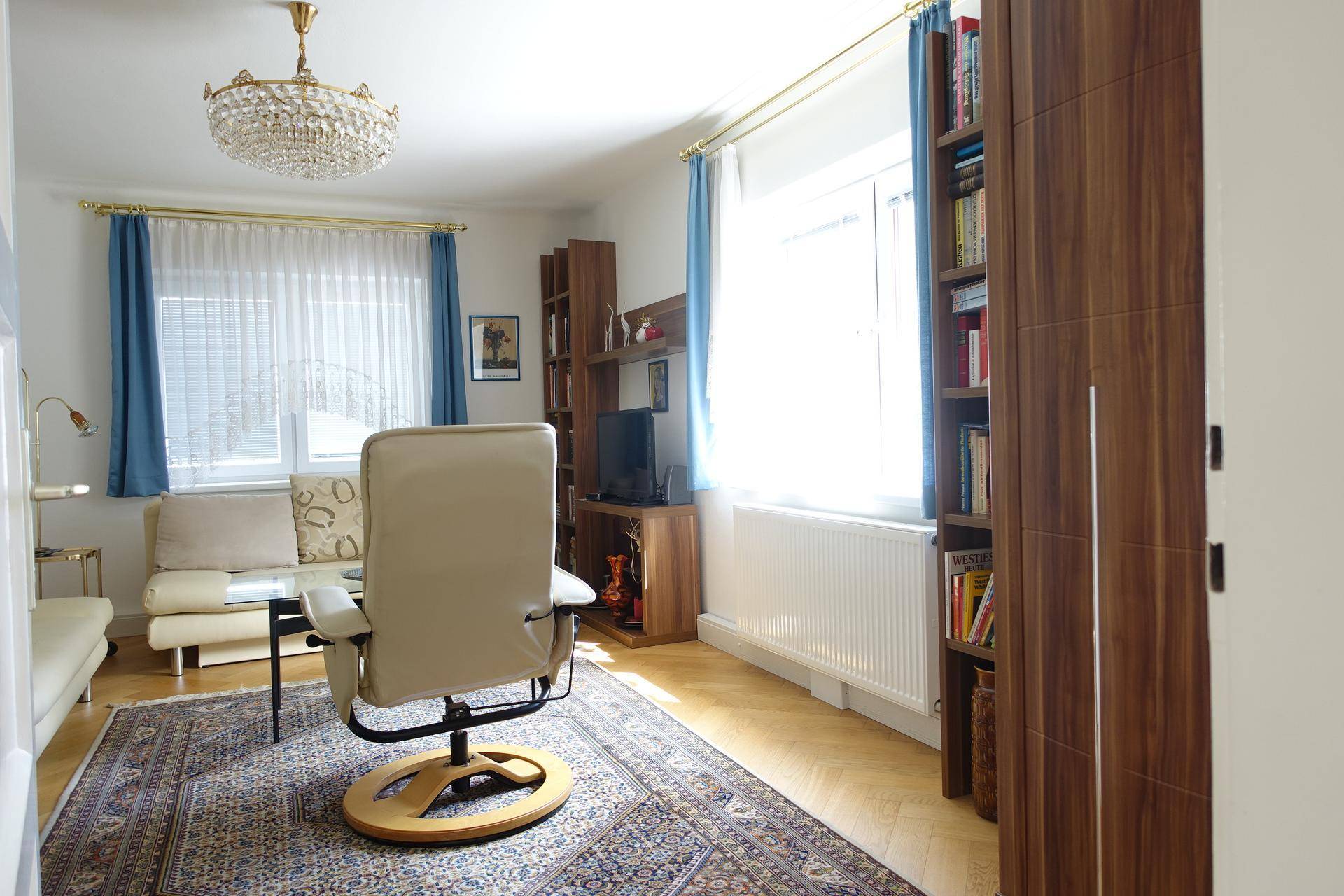 Gemütliches Wohnzimmer mit Schreibtischstuhl, Sofa und Bücherregalen.
