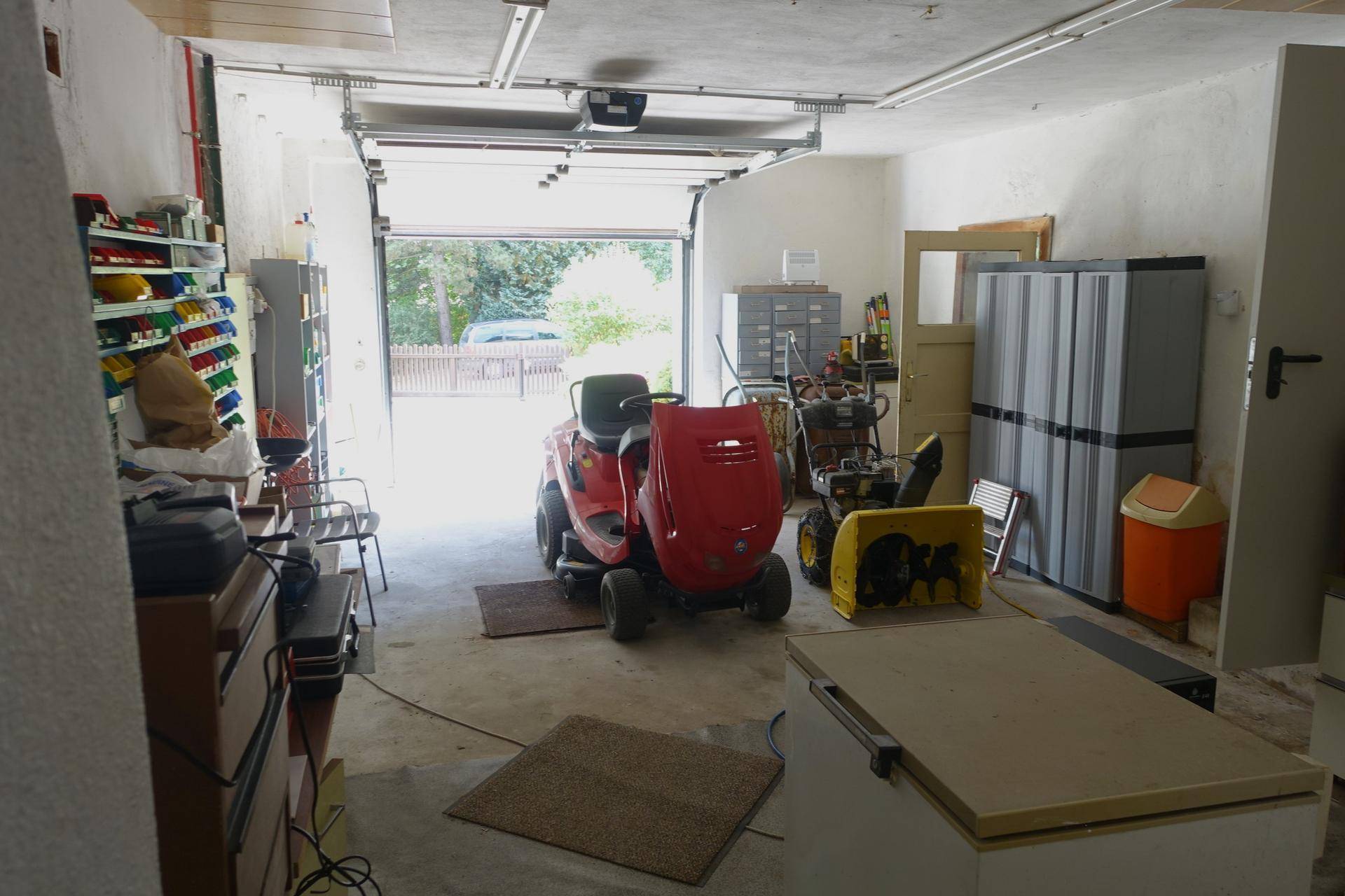 Garage mit offenem Tor, Rasenmäher und Werkzeugen, bietet viel Platz.