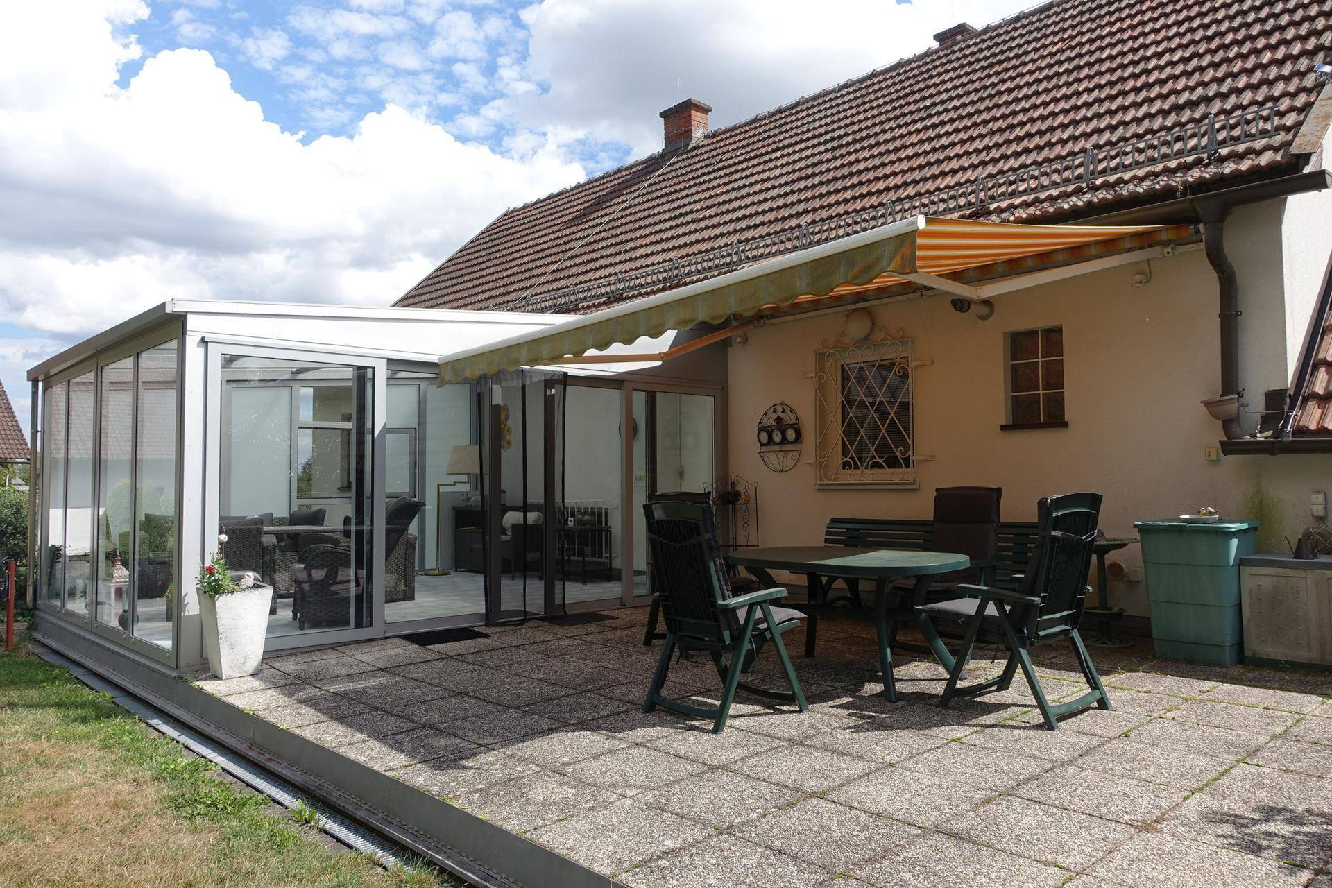 Große gepflasterte Terrasse mit Gartenmöbeln und angrenzendem Wintergarten.