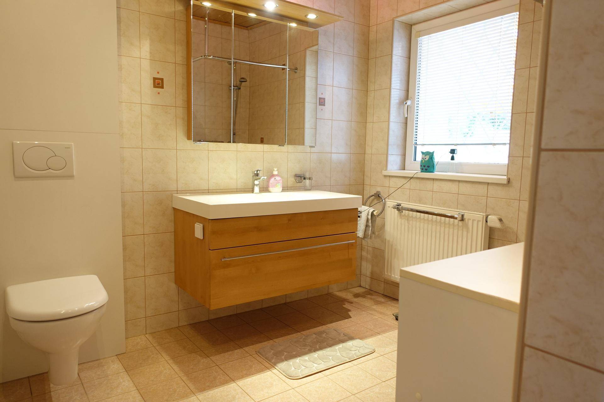 Badezimmer mit modernem Waschbecken, WC und Fenster in hellen Fliesen.