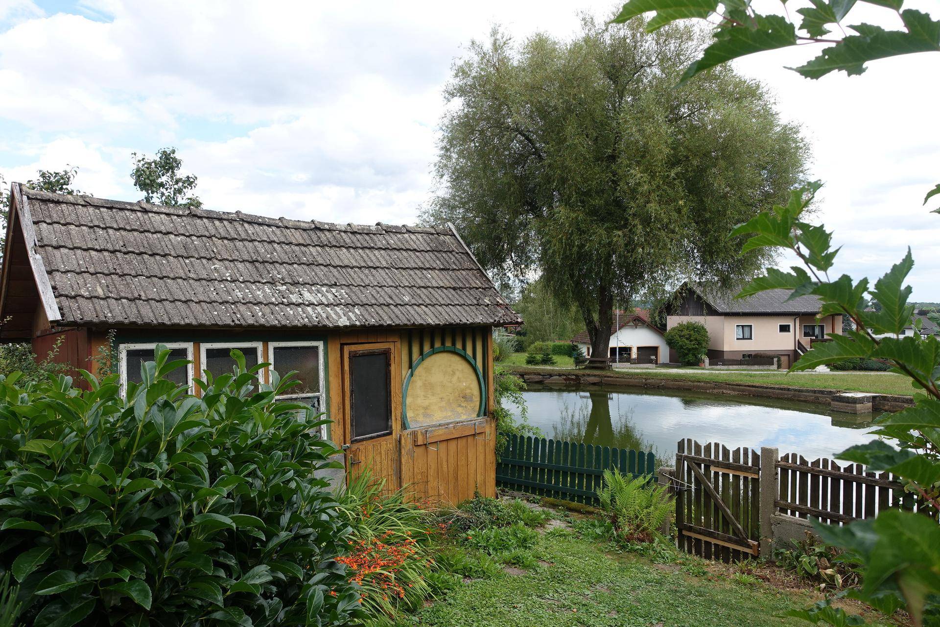 Kleines Holzhaus am Teich mit Blick auf weitere Gebäude und Bäume.