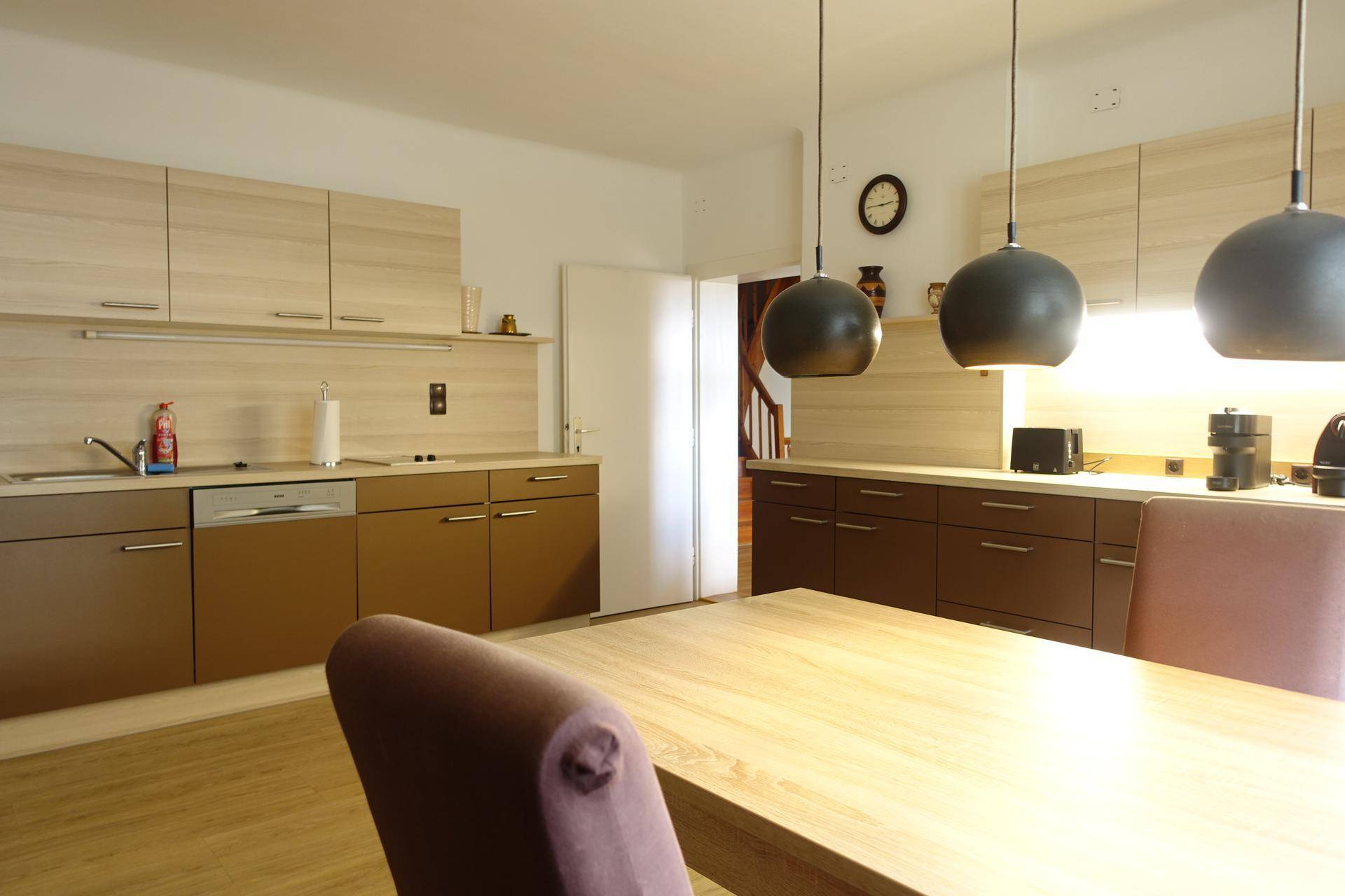 Geräumige Küche mit Holzschränken, Esstisch und modernen Pendelleuchten.