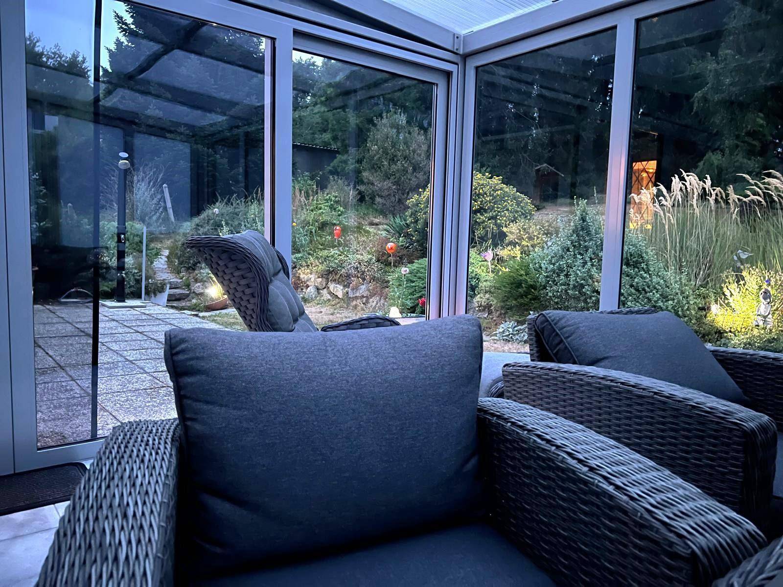 Heller Wintergarten mit bequemen Korbsesseln und Blick auf den Garten in der Abenddämmerung.
