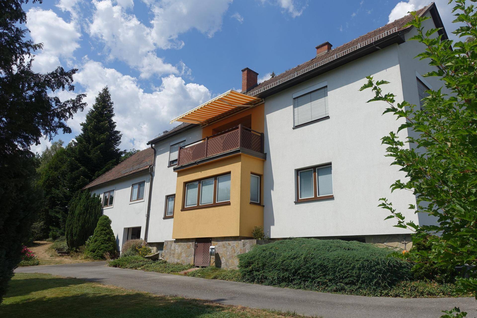 Fassade eines Wohnhauses mit Balkon und Markise unter blauem Himmel.
