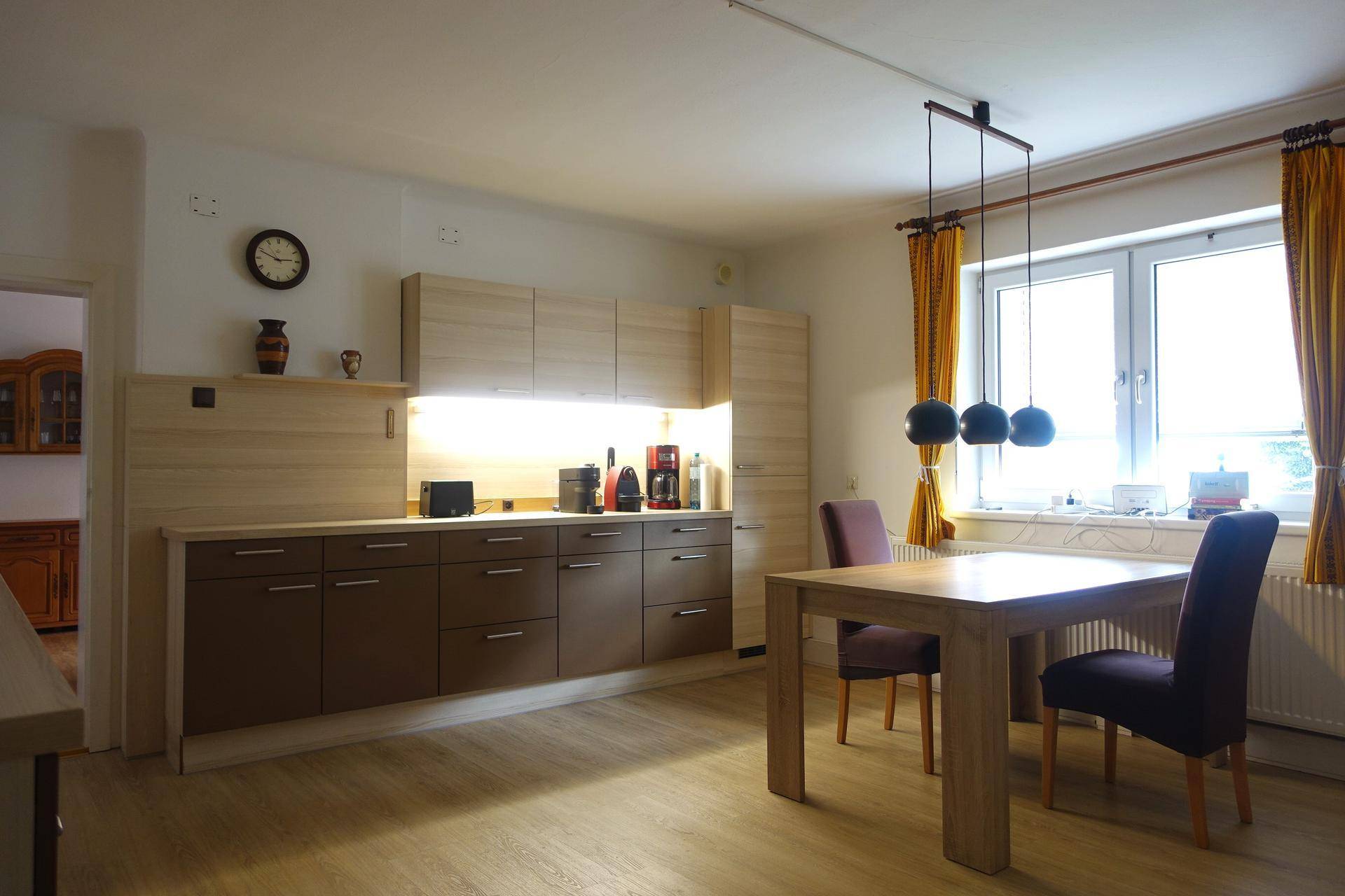 Helle Küche mit Holzschränken, Esstisch und großem Fenster.
