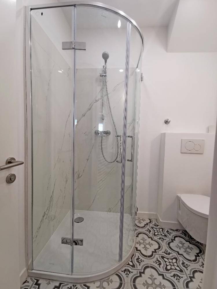 Elegantes Badezimmer mit moderner Duschkabine und gemusterten Bodenfliesen, die einen besonderen Akzent setzen.