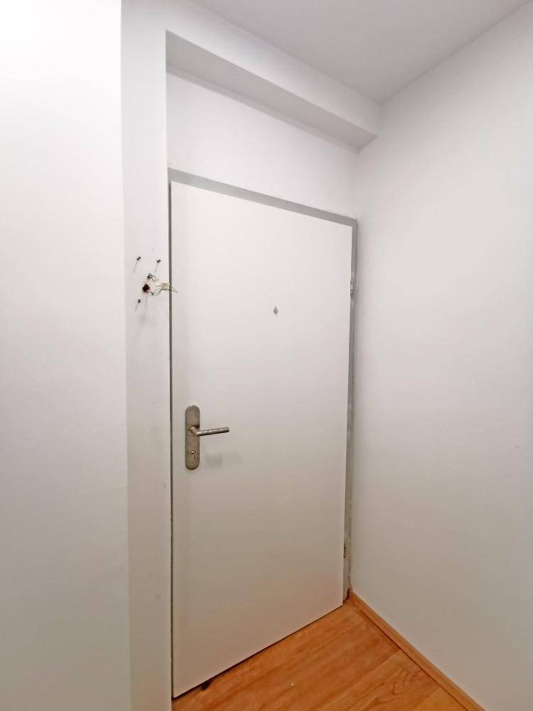 Eingangsbereich mit weißer Tür und Holzboden, der zu den Wohnräumen führt.