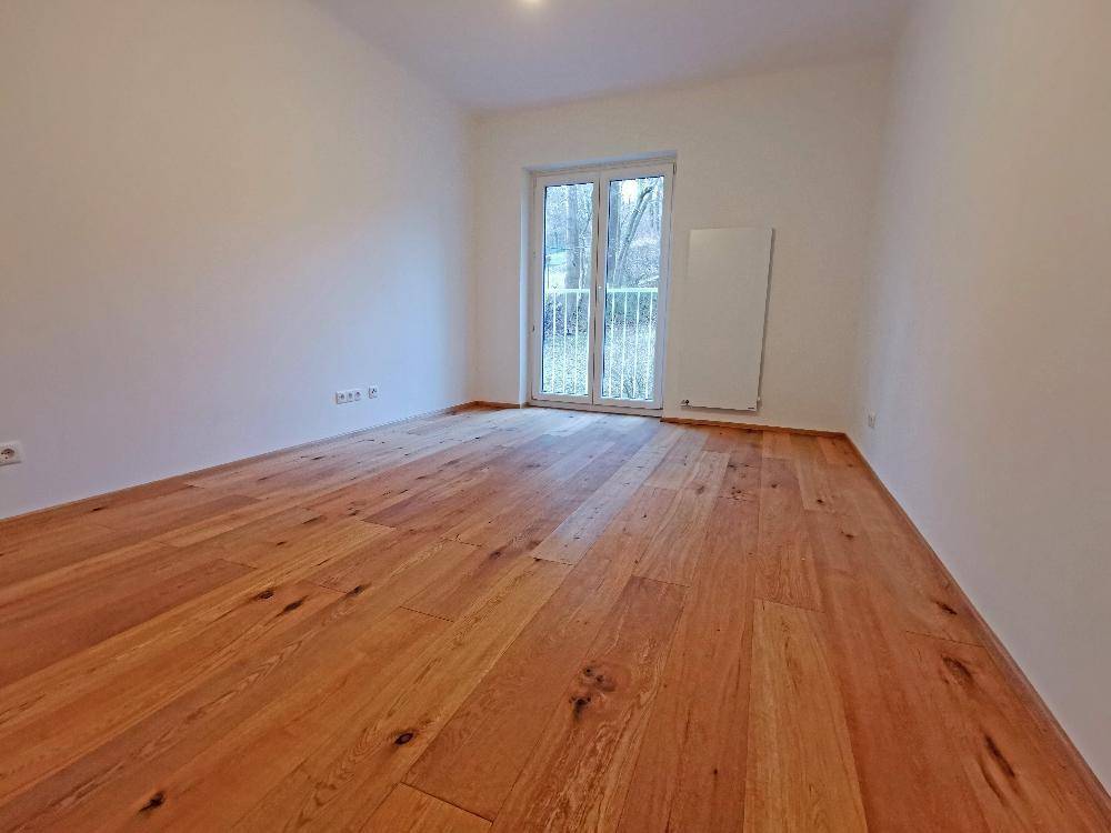 Ruhiges Schlafzimmer mit Holzboden und einem französischen Balkon, der viel Tageslicht hereinlässt.