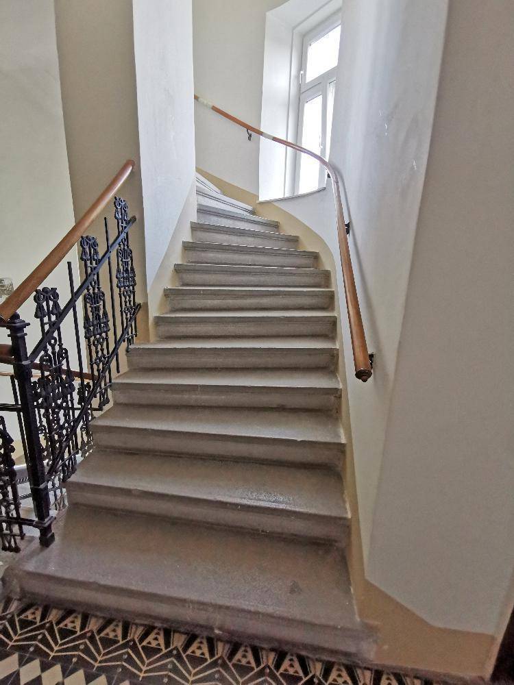 Historisches Treppenhaus mit Steinstufen, schmiedeeisernem Geländer und Holzhandlauf.