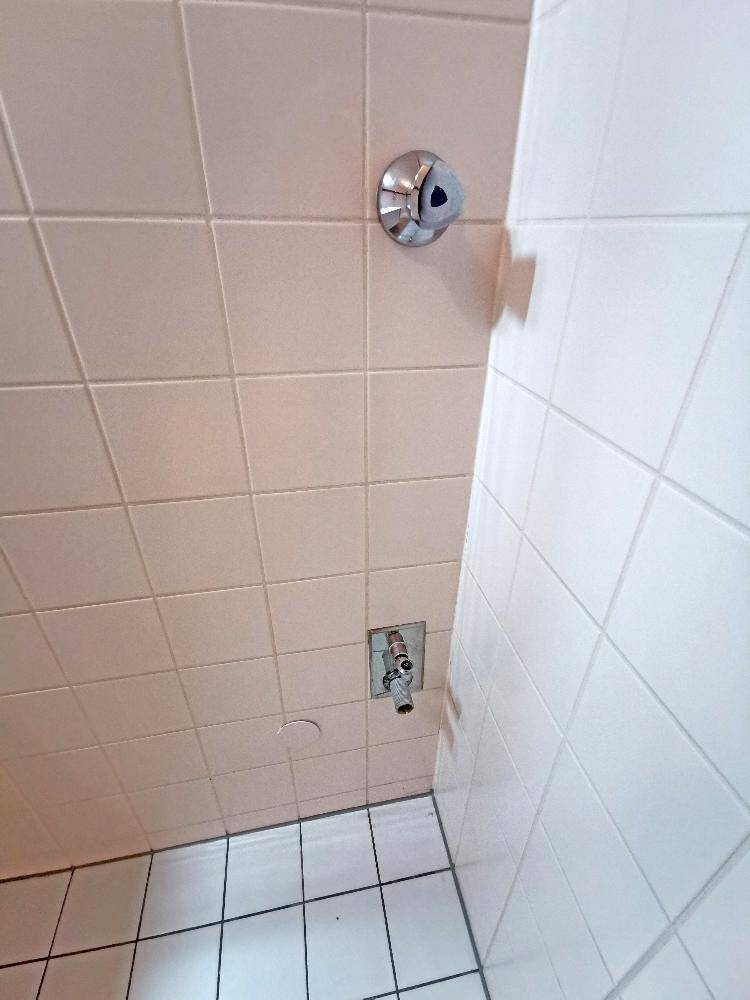 Nahaufnahme der Duscharmatur in einem gefliesten Badezimmer, zeigt einfache und funktionale Ausstattung.