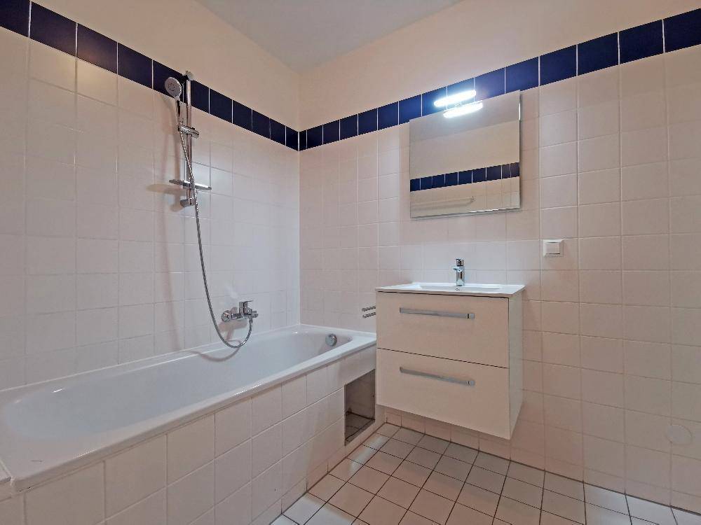 Badezimmer mit Badewanne, Waschbecken und weißen Fliesen, akzentuiert durch eine blaue Bordüre.