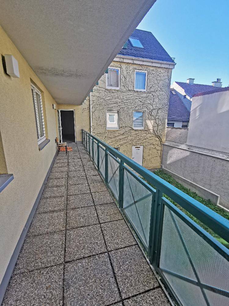 Langer Balkon mit Fliesenboden und Blick auf die umliegenden Gebäude und den Innenhof.