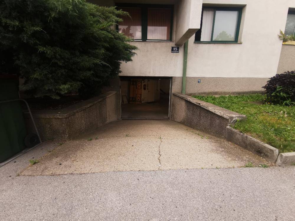 Einfahrt zur Tiefgarage mit Betonrampe und umgebender Grünfläche.